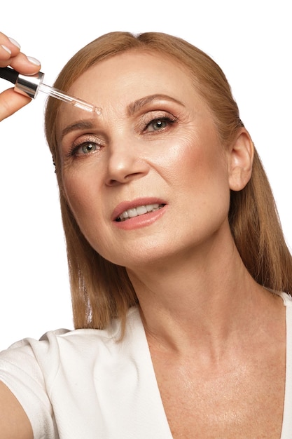 Retrato de una hermosa anciana con una camisa blanca con aceite facial cosmético en las manos