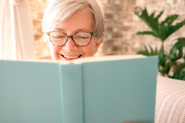 Retrato de una hermosa anciana caucásica con anteojos parcialmente ocultos por un concepto de libro de dama relajada disfrutando de la lectura de jubilación