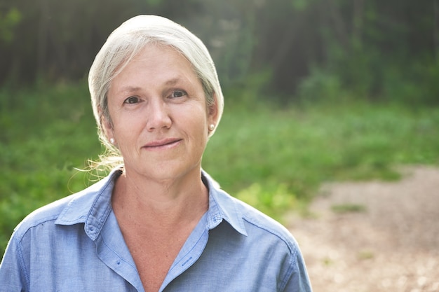 Foto retrato de hermosa anciana de pelo gris sonriendo en el fondo del parque