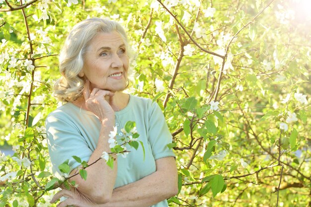 Retrato de una hermosa anciana posando cerca de un árbol floreciente