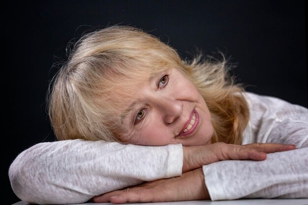 Foto retrato de una hermosa anciana una rubia sonriente se sienta con la cabeza soñadora en sus manos feliz madurez closeup fondo negro