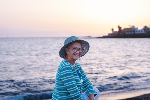 Retrato de una hermosa anciana sentada en la playa a la luz del atardecer anciana mirando a la cámara sonriendo disfrutando de la relajación y la belleza en la naturaleza