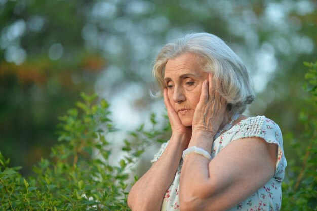 Retrato de hermosa anciana triste en el parque de verano