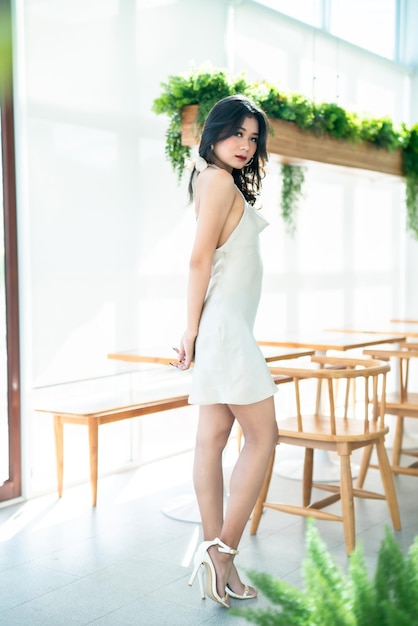 Retrato hermosa asiática freelance Gente de éxito modelo de moda de mujer de negocios en vestido sin mangas blanco de verano y café en taza en cafetería