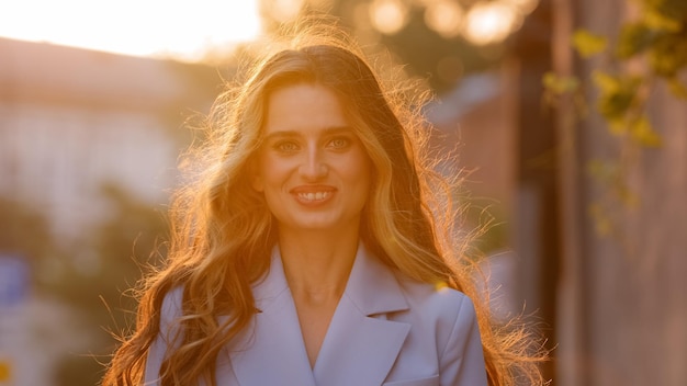 Retrato hermosa atractiva chica caucásica feliz con cabello largo se encuentra rayos de sol mirando de fondo