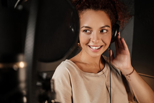 Retrato de una hermosa cantante escuchando sonido en auriculares trabajando en un nuevo álbum de música en un estudio de grabación moderno