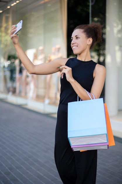 Retrato de una hermosa chica americana con coloridos paquetes de papel tomando selfies en su teléfono