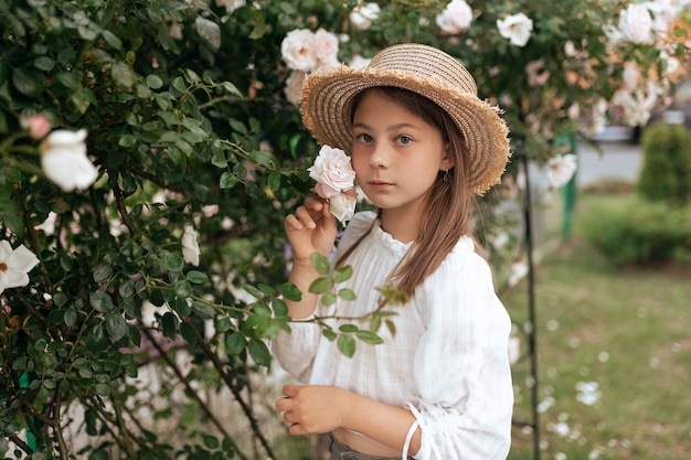 Retrato de una hermosa chica con cabello largo y pecas en un sombrero de paja afuera en verano cerca de rosas