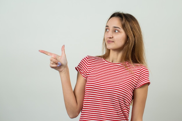 El retrato de una hermosa chica con una camiseta a rayas mira a un lado con una expresión pensativa y está considerando un plan de acción adicional