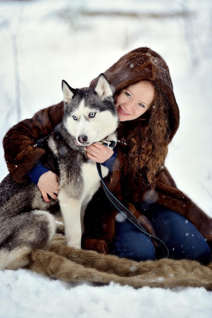 Retrato de una hermosa chica en una capucha de piel en un día de invierno con un perro Husky en el Parque