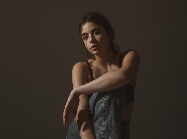 Retrato de una hermosa chica elegante en sujetador negro y jeans sentado y mirando a la cámara