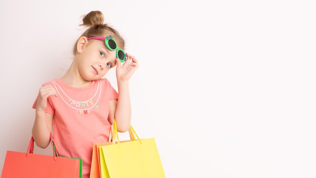 Retrato de una hermosa chica emocionada con vestido y gafas de sol sosteniendo bolsas de compras aisladas