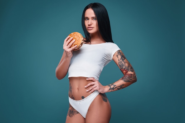 Retrato de hermosa chica encantadora tatuaje sosteniendo hamburguesa