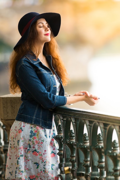 Retrato de la hermosa chica de moda con sombrero en terraplén en día de verano