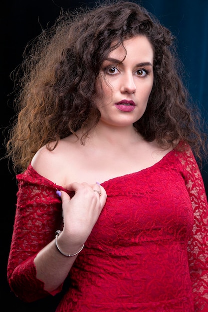 Retrato de una hermosa chica morena con el pelo rizado con un vestido rojo sobre un fondo oscuro.