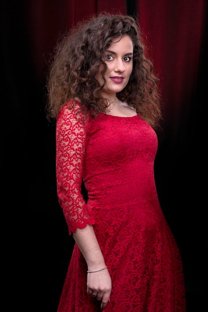 Retrato de una hermosa chica morena con el pelo rizado con un vestido rojo sobre un fondo oscuro.