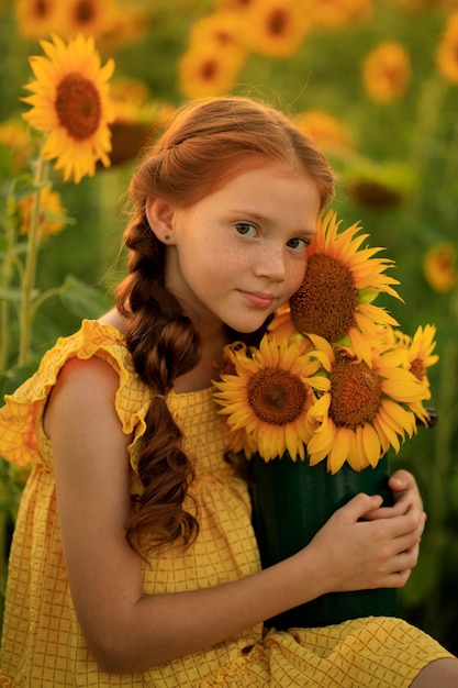 Retrato de una hermosa chica pelirroja con coletas con un ramo de girasoles en sus manos verano en el pueblo un campo de girasoles