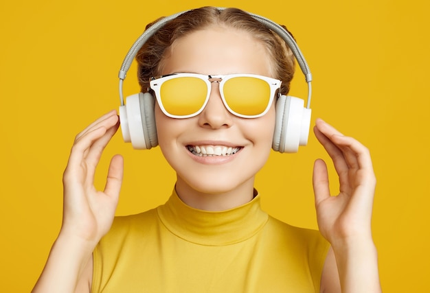 Retrato de hermosa chica rubia hipster con pelo rizado con gafas de sol disfruta de la música en auriculares sobre fondo amarillo