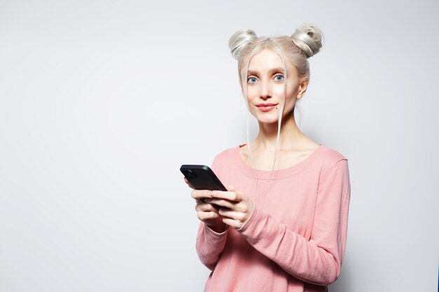 Retrato de hermosa chica rubia con moños de pelo smartphone en manos en blanco