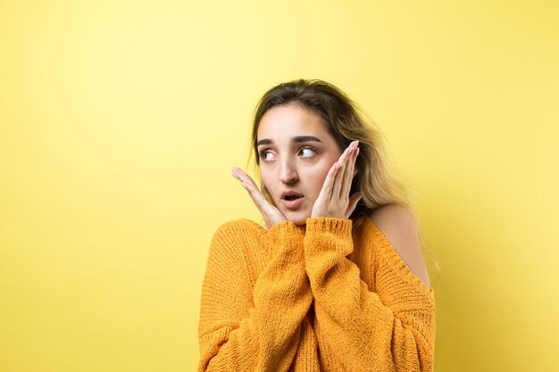 El retrato de una hermosa chica con un suéter naranja mira a un lado con una expresión pensativa y está considerando un plan de acción adicional