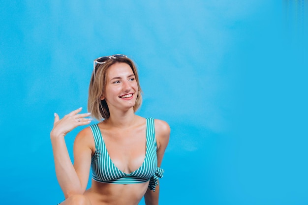 Retrato de una hermosa chica en traje de baño, la chica está sonriendo y tiene una foto de gafas de sol en una playa de fondo azul, vacaciones de verano