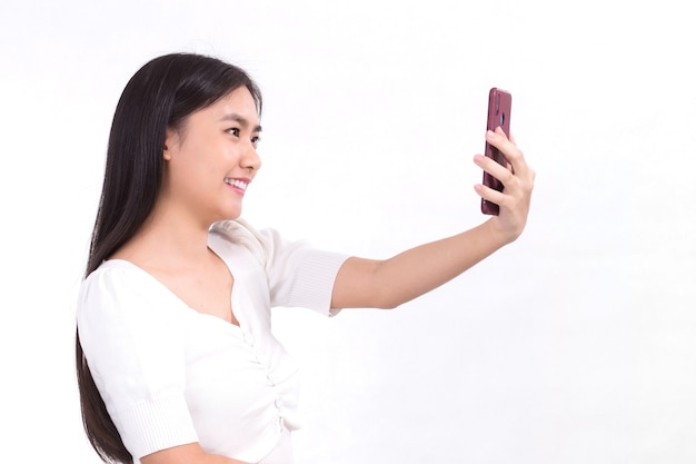 Retrato de hermosa dama asiática que tiene el pelo largo negro con camisa blanca sostiene el teléfono inteligente