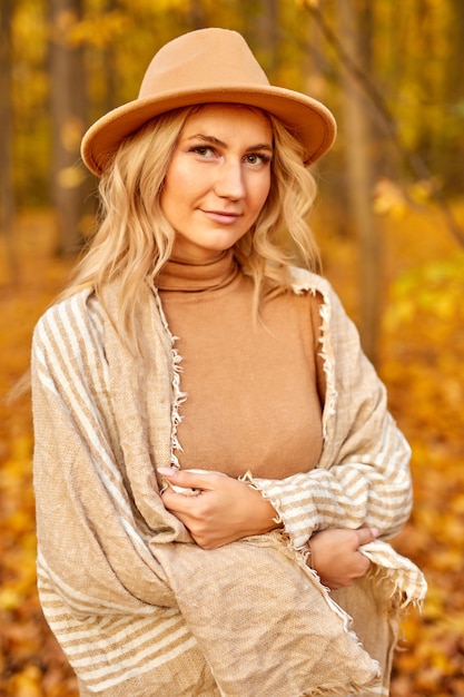 Retrato de hermosa dama con sombrero posando a la cámara en la naturaleza otoñal