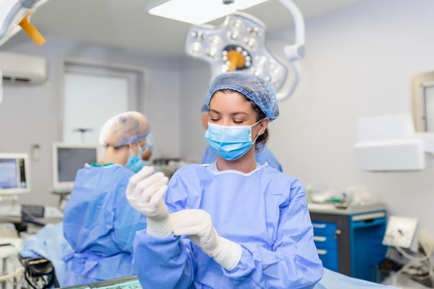 Retrato de una hermosa doctora cirujana poniéndose guantes médicos de pie en el quirófano Cirujano en el quirófano moderno