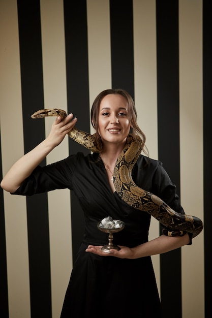 Retrato de una hermosa doctora cosmetóloga con serpiente sosteniendo un tazón con preparaciones médicas para inyección en la clínica moderna Símbolo de la medicina