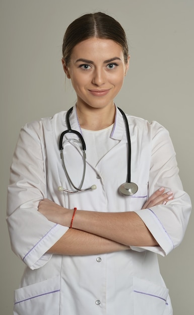 Retrato de hermosa doctora con estetoscopio, de pie sobre fondo gris