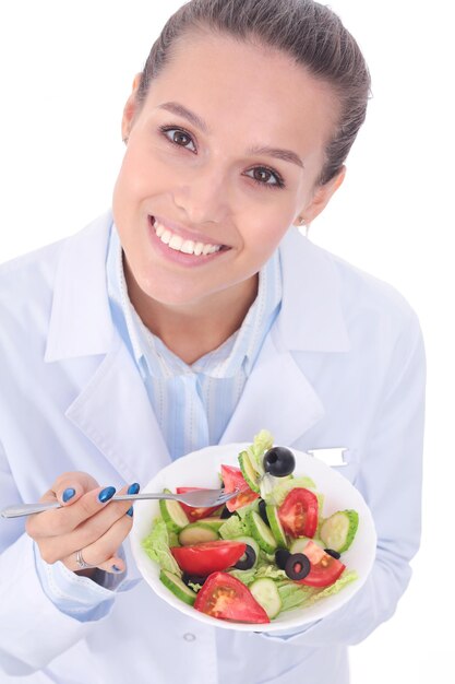 Retrato de una hermosa doctora sosteniendo un plato con verduras frescas