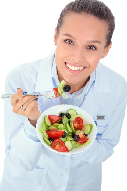 Retrato de una hermosa doctora sosteniendo un plato con verduras frescas