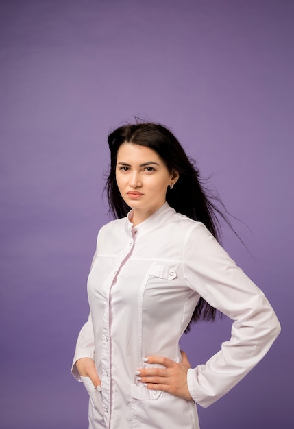 Retrato de una hermosa doctora en un uniforme blanco sobre púrpura