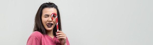 Retrato de hermosa dulce hermosa mujer alegre con cabello castaño lacio tratando de morder bastón de caramelo rojo navidad