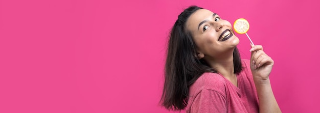 Retrato de una hermosa y dulce mujer alegre con cabello castaño lacio sosteniendo una piruleta cerca de los ojos