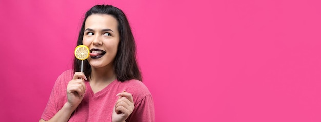 Retrato de una hermosa y dulce mujer alegre con cabello castaño lacio sosteniendo una piruleta cerca de los ojos