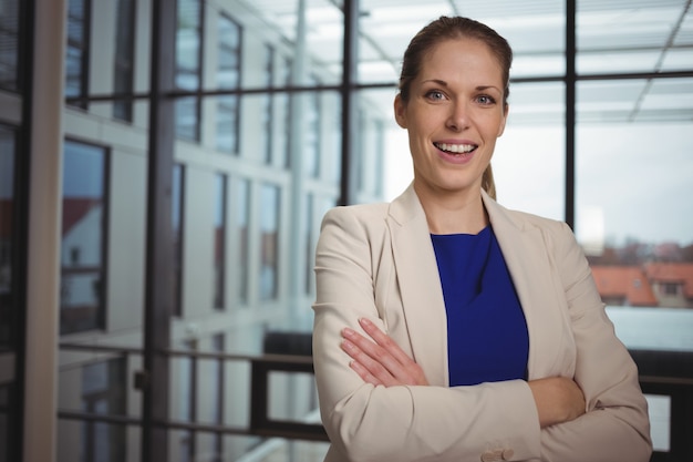 Retrato de hermosa empresaria de pie con los brazos cruzados en el pasillo