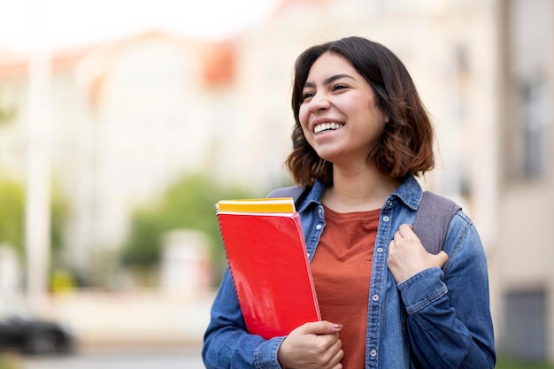 Retrato de una hermosa estudiante árabe con libros de trabajo en la mano posando al aire libre