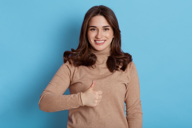 Retrato de hermosa estudiante de cabello oscuro con amplia sonrisa, mirando a la cámara con expresión feliz