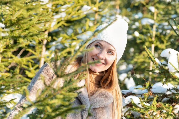 Retrato de una hermosa joven con un abrigo de piel y sombrero sobre el fondo del bosque de invierno