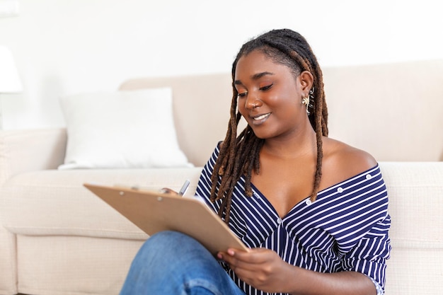 Foto retrato de hermosa joven africana trabajando en casa mujer sentada y escribiendo notas