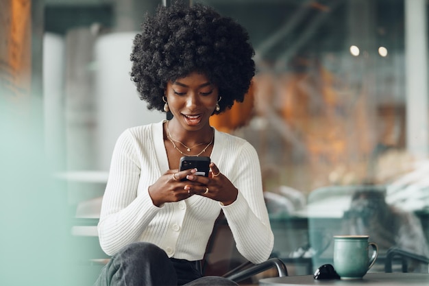 Retrato de una hermosa joven africana usando su teléfono móvil en un café