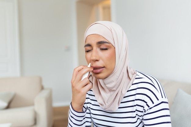 Foto retrato de una hermosa joven árabe musulmana olfateando spray nasal cerrando una nariz primer plano de una mujer que se siente enferma con la nariz que corre usando medicación sinusal para la nariz bloqueada