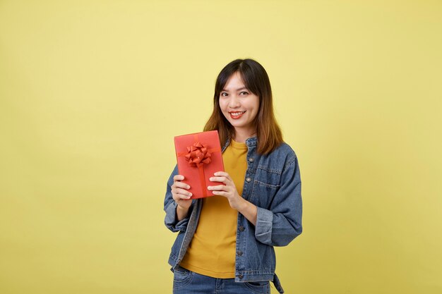 Retrato hermosa joven asiática con caja de regalo roja sobre amarillo aislado