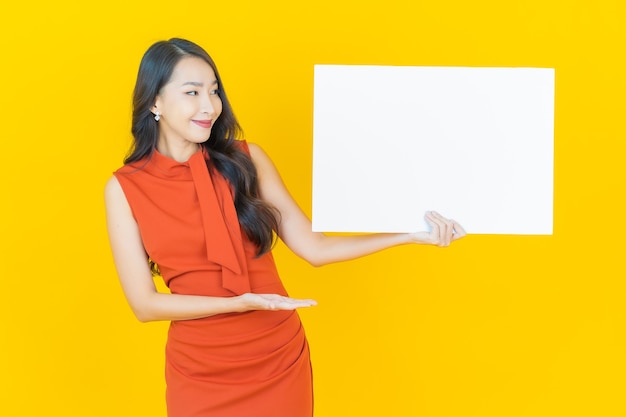 Retrato hermosa joven asiática con cartelera blanca vacía en amarillo