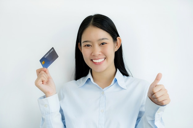 Retrato de una hermosa joven asiática hermosa con cabello largo sosteniendo una tarjeta de crédito azul, sus ojos brillando a la cámara. Listo para pagar comprando según productos con descuento.