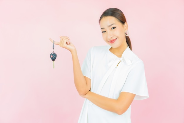 Retrato hermosa joven asiática con llave de coche en la pared de color rosa