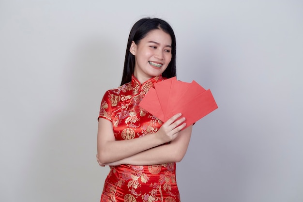 Retrato hermosa joven asiática llevar un vestido chino con paquete rojo regalo monetario de felicitación saludo feliz año nuevo 2021 aislado sobre fondo gris claro con espacio de copia