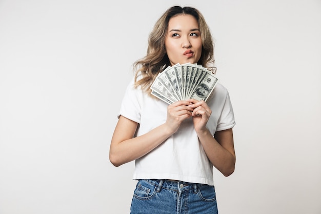 Retrato de una hermosa joven asiática que se encuentran aisladas sobre una pared blanca, mostrando billetes de dinero