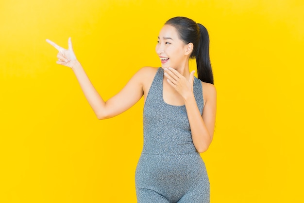 Retrato hermosa joven asiática con ropa deportiva lista para hacer ejercicio en la pared amarilla